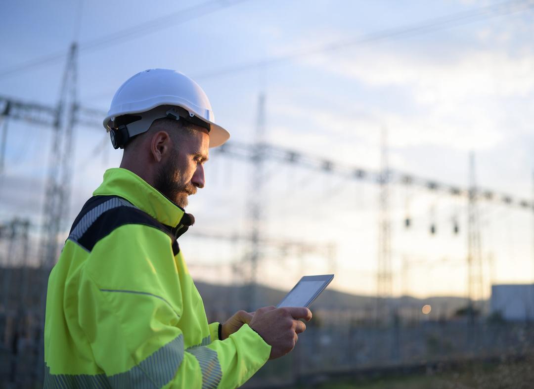 An engineer in a hard hat and safety vest is consulting a tablet.