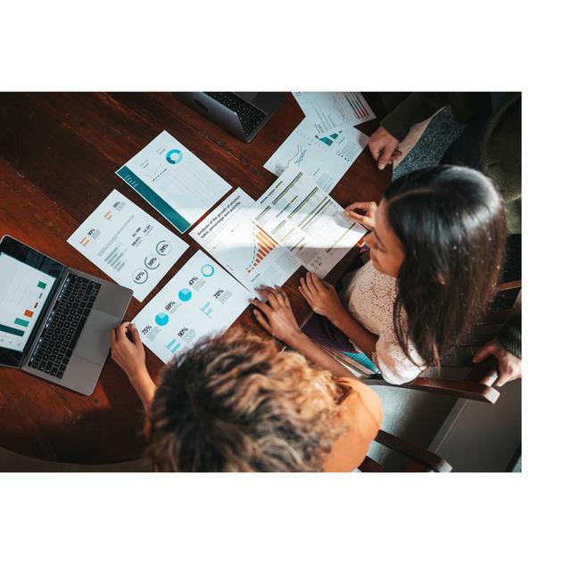 An overhead photo fo women consulting data charts on papers as well as a laptop.