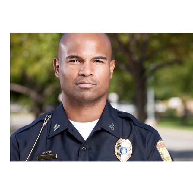 A male police officer is standing outside, shown looking directly at the camera. The image is a close-crop view, from the chest up.