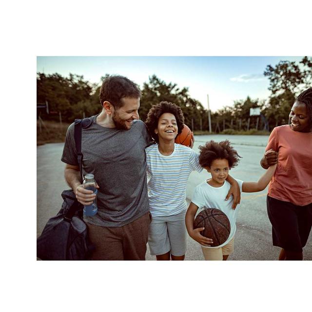 A family smiles and laughs as they walk together, holding basketballs on a basketball court.