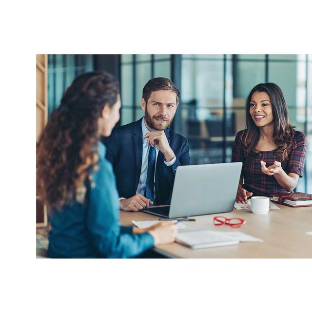 A man and two women sit together at a conference table, collaboratively chatting in an office.