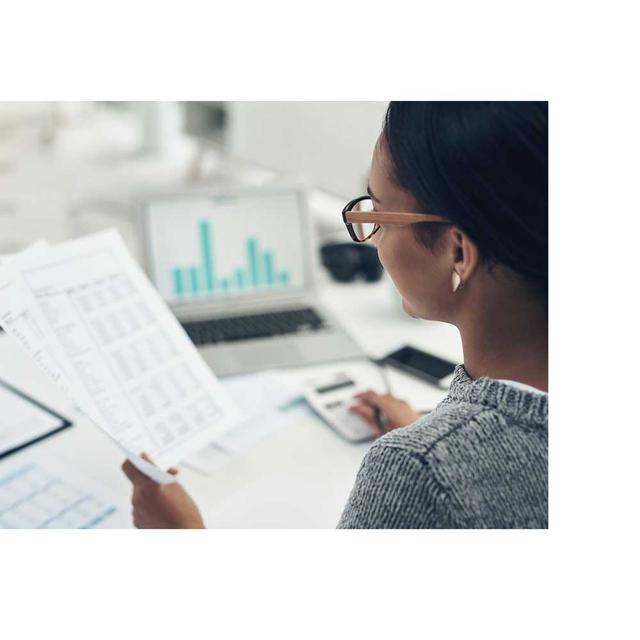 A woman holds paper and enters numbers into a calculator, managing a budget.