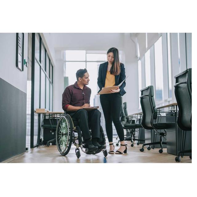 A man in a wheelchair and a woman standing next to him review a file held by the woman in an office setting.