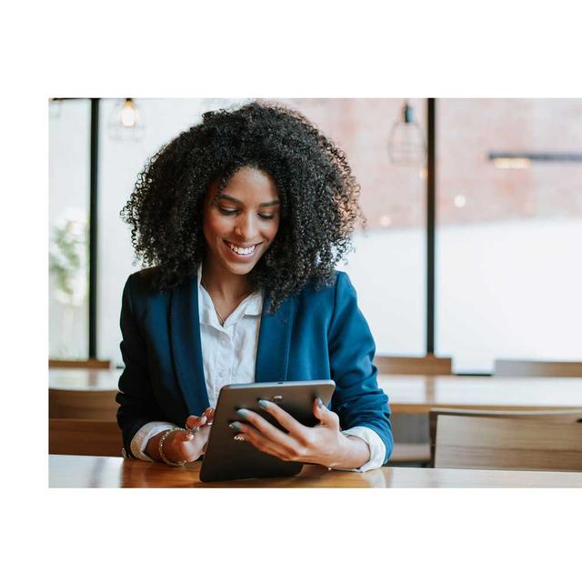 A woman smiles as she uses a tablet in an office setting.