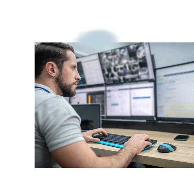 A male telecommunicator sits at a desk in front of many computer monitors, typing on a keyboard as he interacts with CentralSquare's Vertex NG911 Call Handling Solution.