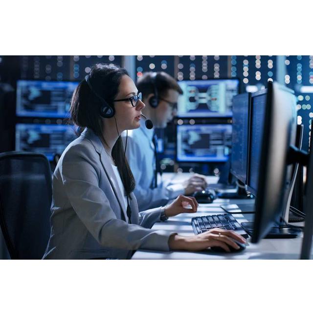 Two IT workers in a blue-lit room working on separate computers.