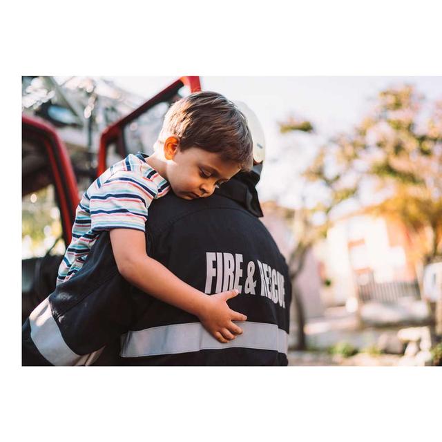 A young boy looks relieved as he is held over the shoulder by a fire and rescue worker, who is facing away from the camera.