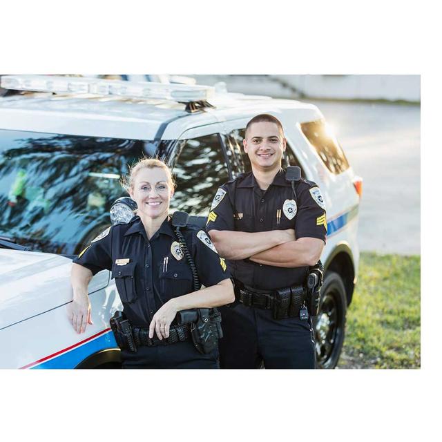 Two public safety law enforcement officers lean on a patrol car, smiling.