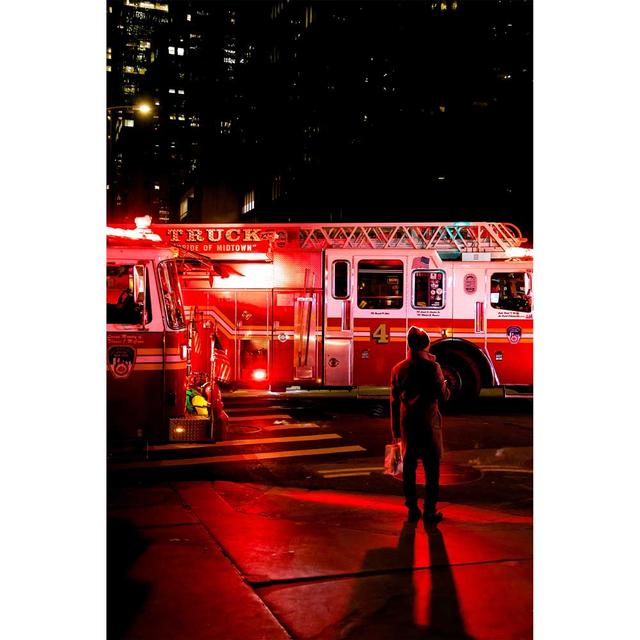 A dramatic photo of a firetruck at night, which is illuminated by the lights of another firetruck that is entering the frame from the left.