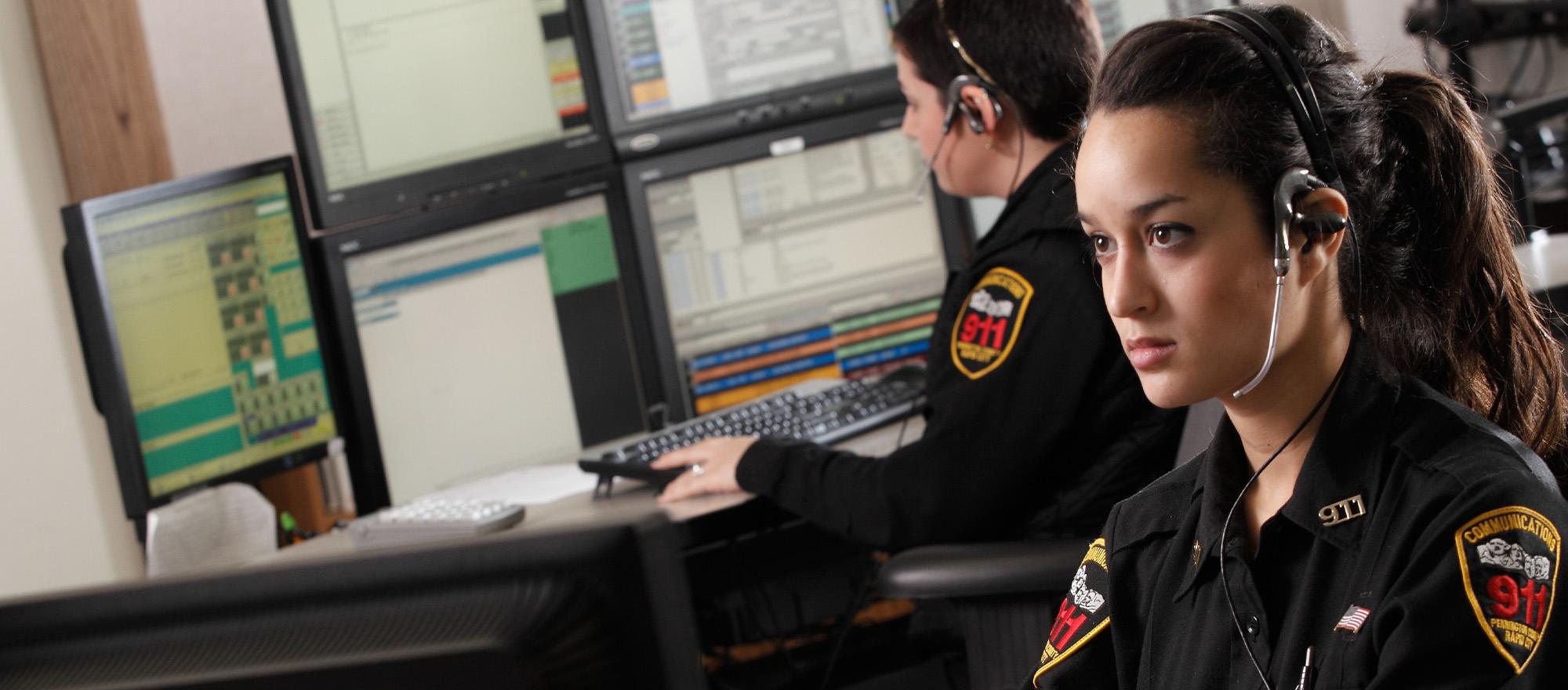 A mobile optimized version of two female telecommunicators wearing headsets are typing on computers. Multiple computer screens display CentralSquare's CAD solution.