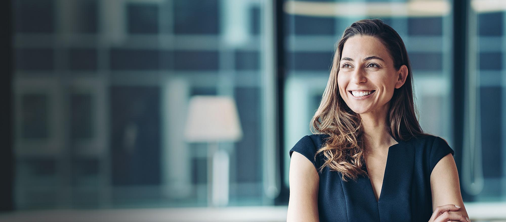 A middle aged woman with medium length light brown hair smiles confidently with her arms crossed in an office setting.