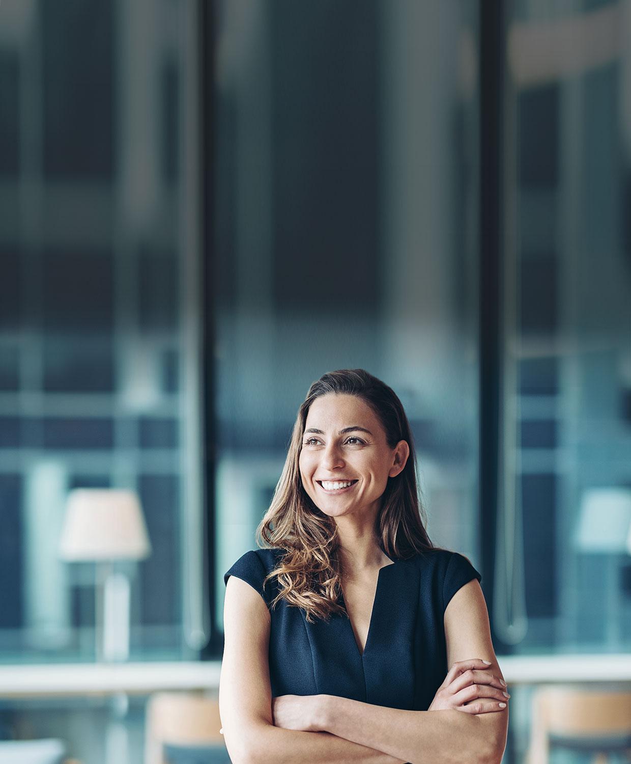 A middle aged woman with medium length light brown hair smiles confidently with her arms crossed in an office setting.