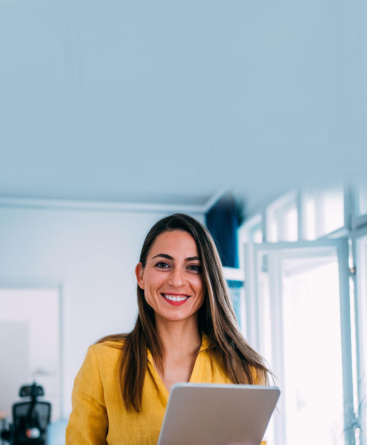 A woman in holds a stack of papers and smiles in an office setting.