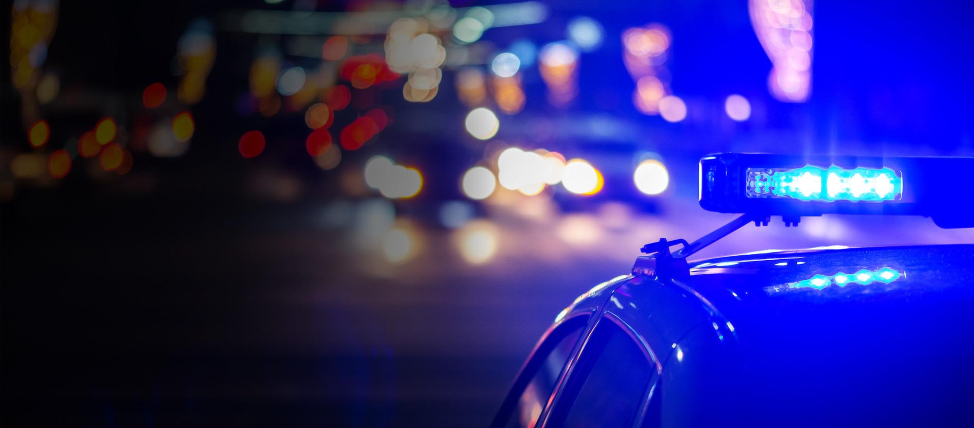 A dramatic photo of a patrol car on a city street at night with its emergency lights on. The car is in focus while the background is less distinguishable.