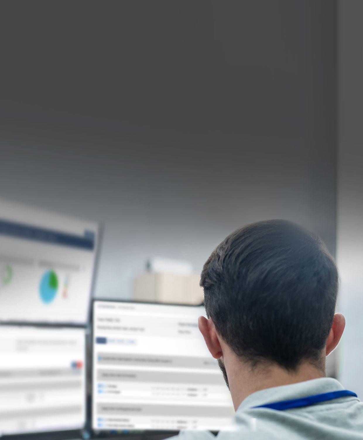 An over the shoulder view of a man working on two desktop screens which display CentralSquare's Field Training solution.