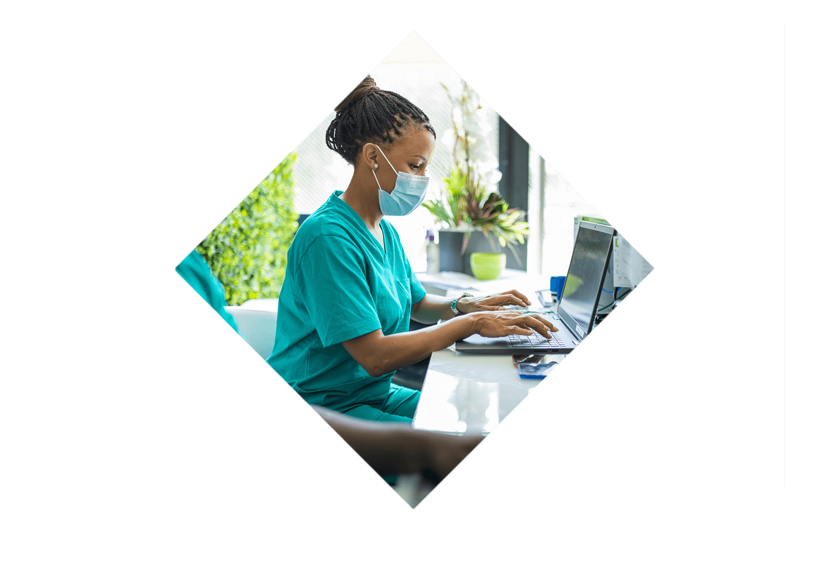 A nurse wearing a mask types at a laptop.