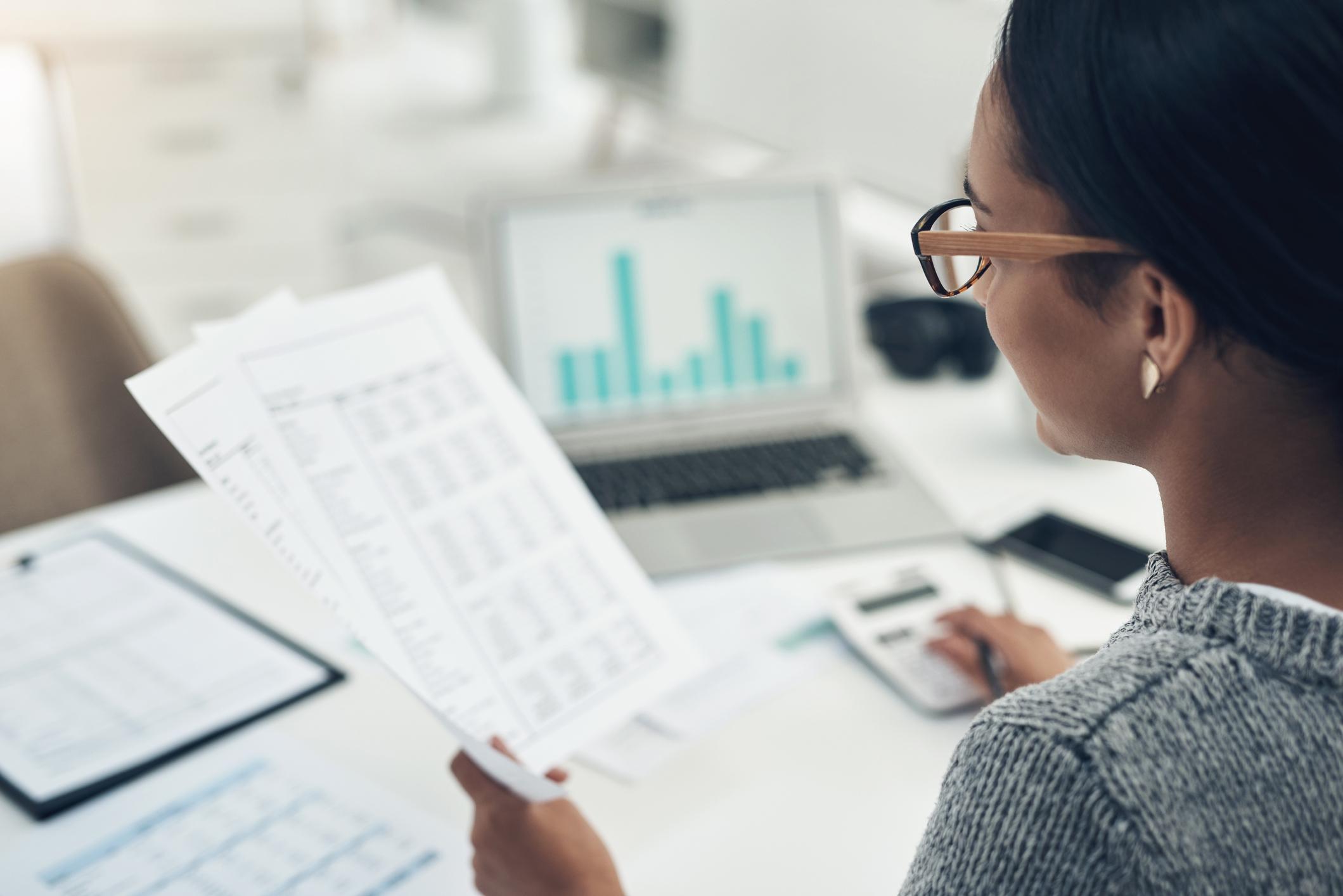 A businesswoman is seen managing a budget, holding papers and inputting numbers into a calculator.