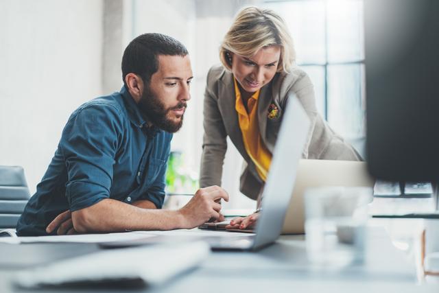 A man and a woman consult a laptop together, where they are managing city assets and finances.