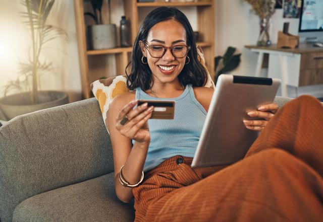 A woman smiles as she is seen using self-service technology to complete a payment on her tablet from her couch at home.