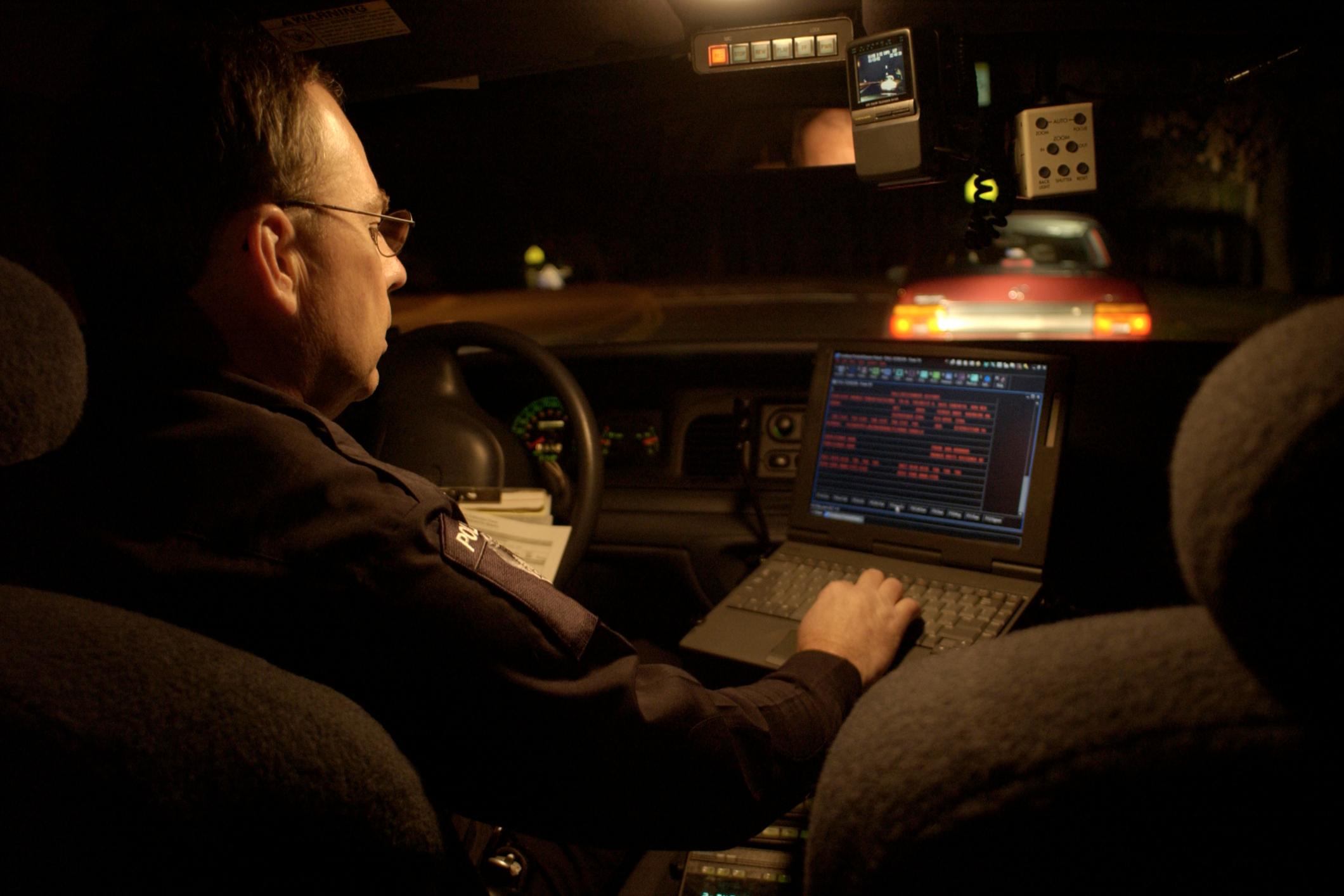 A police officer entering data on a laptop in his vehicle.