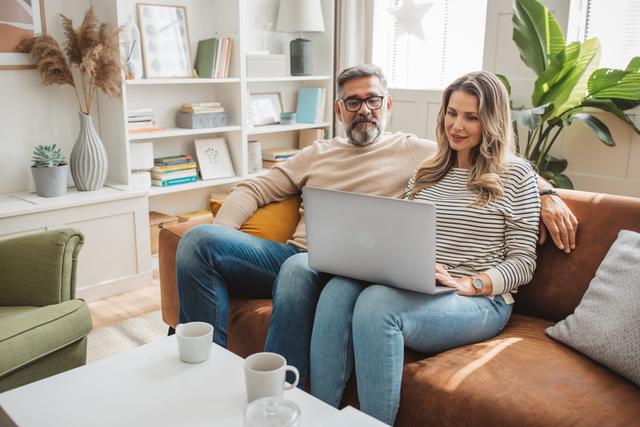 A middle-aged couple looking at a laptop together on a sofa.