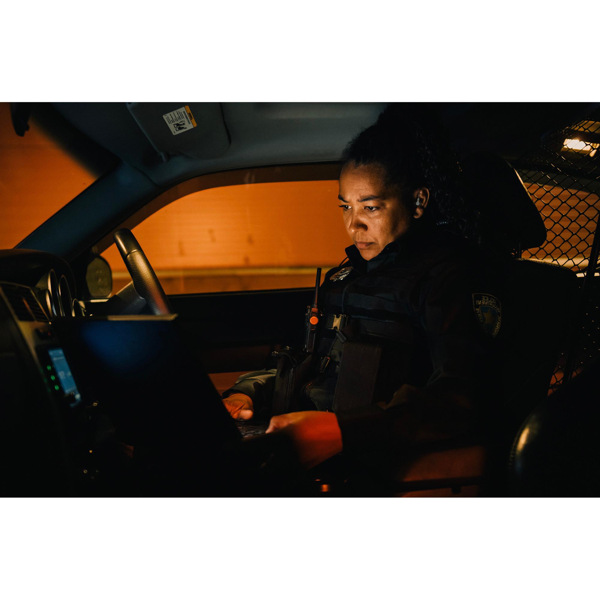 A woman officer in a patrol car looking at a computer screen