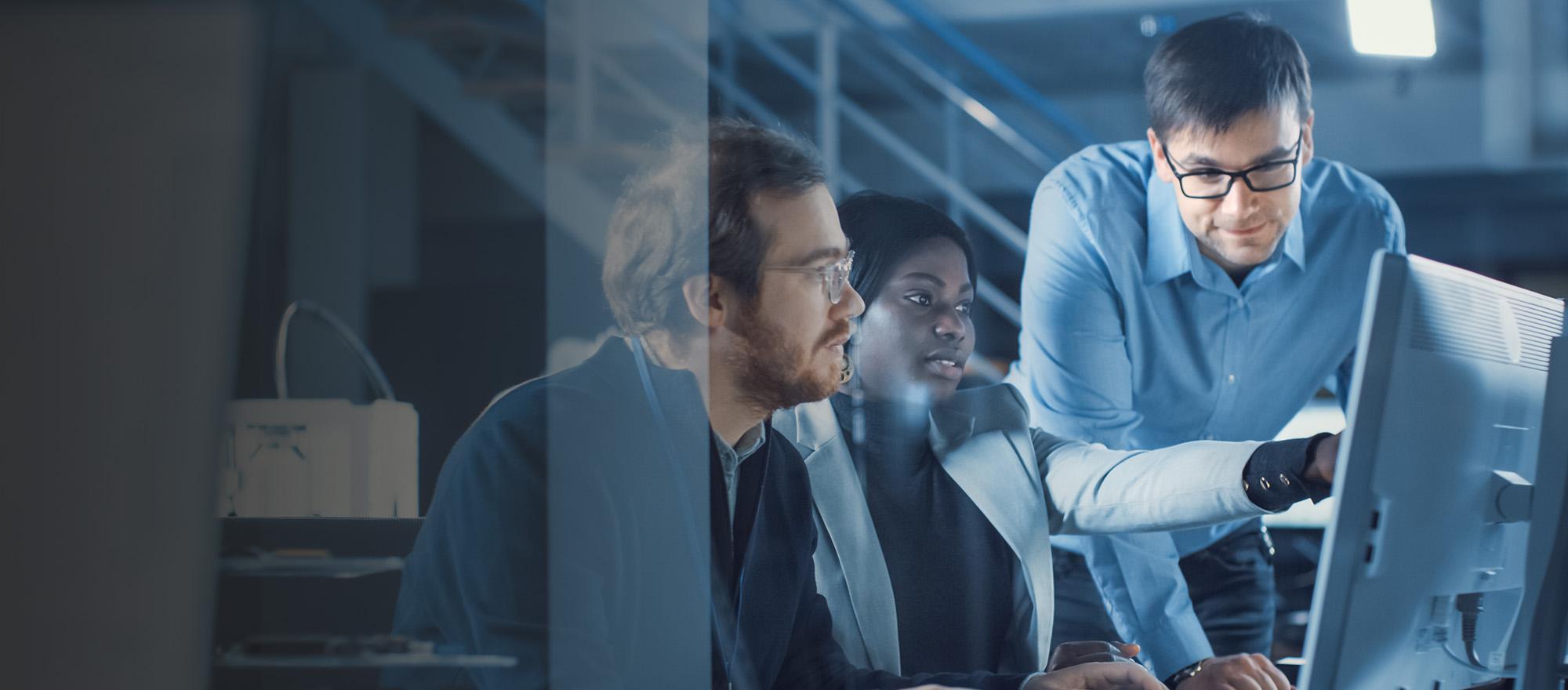 Three co-workers working together in front of a computer screen