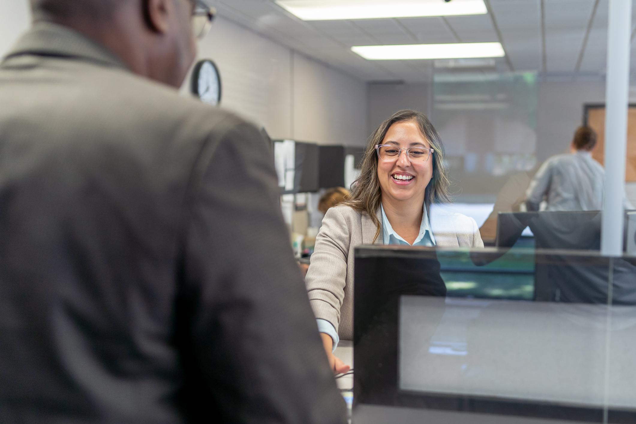 A female employee smiles while greeting a male customer at the reception desk